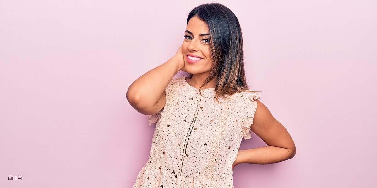 Smiling model posing against pastel pink background.