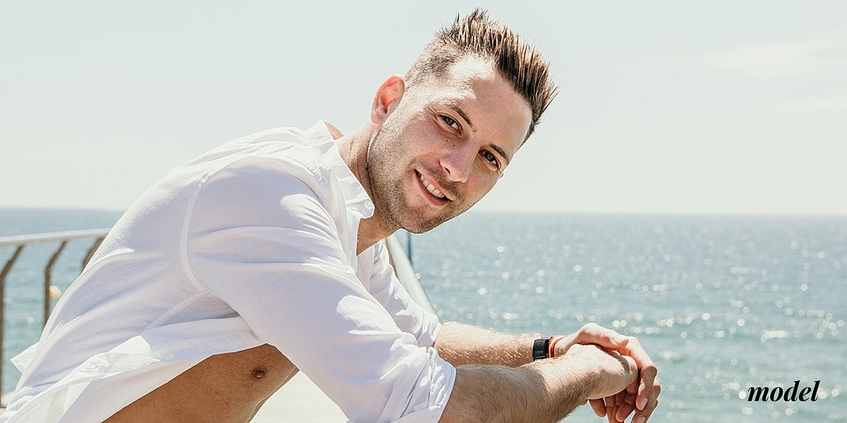 Smiling man by the ocean in white shirt.