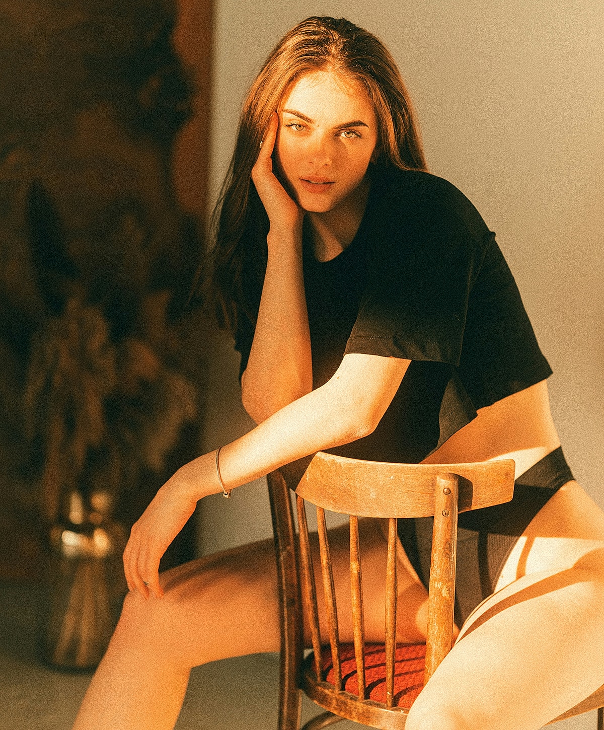 Model seated on a wooden chair, sunlit portrait.