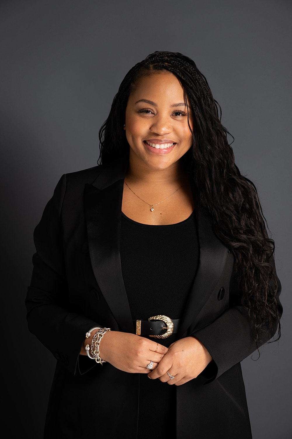 Woman smiling in a black suit against gray background.