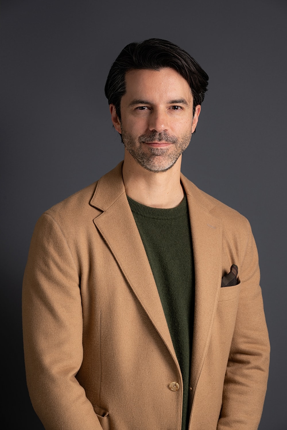 Man in tan coat with green sweater.