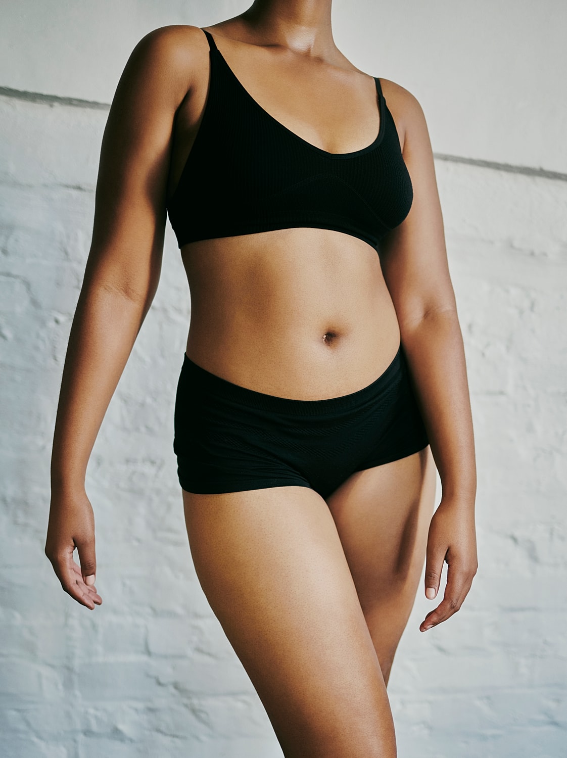 Model in black lingerie against a textured wall.
